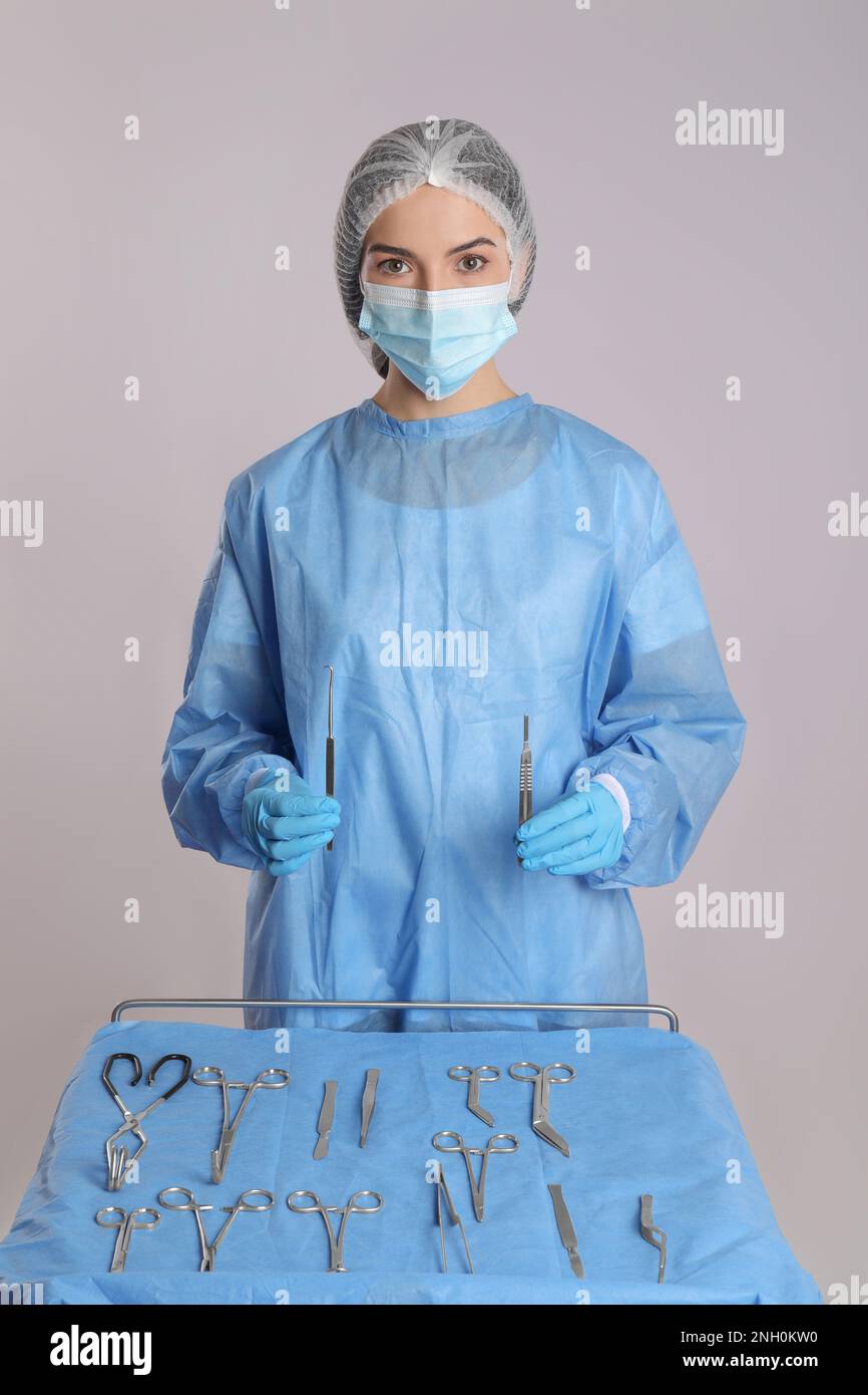 Doctor holding surgical instruments near table on light background ...