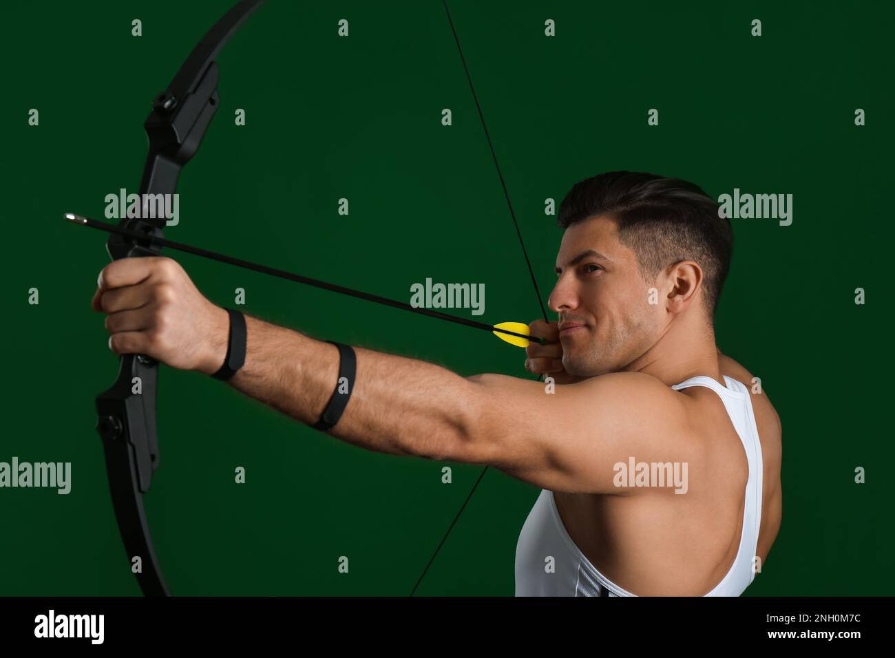 Man with bow and arrow practicing archery on green background Stock Photo