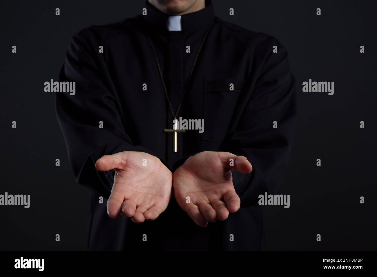 Priest reaching out his hands on black background, closeup Stock Photo