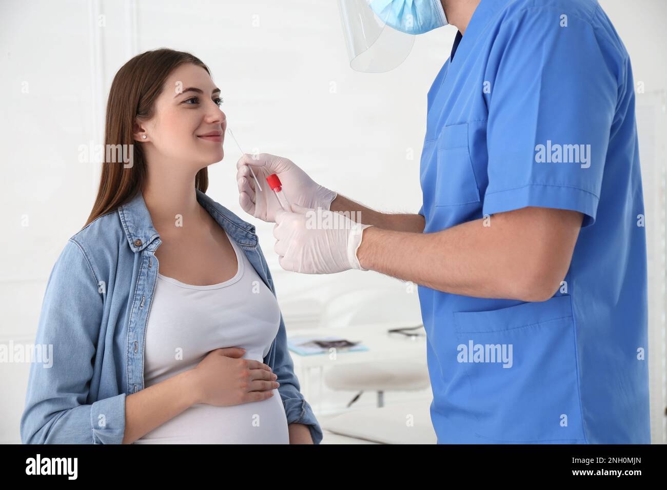 Doctor taking nasal smear of pregnant woman for coronavirus test in clinic Stock Photo