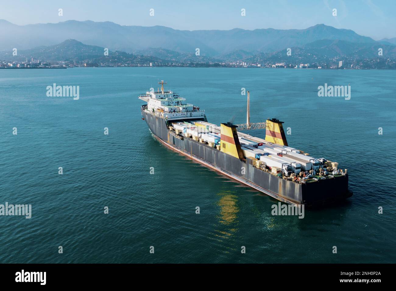 Cargo freight ship with containers and trucks sailing to industrial logistic port, aerial view