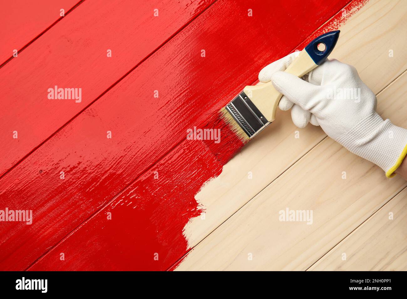 Worker in gloves painting wooden surface with red dye, top view. Space