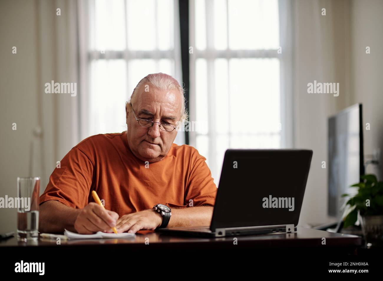 Senior man watching educational video on laptop and taking notes Stock Photo
