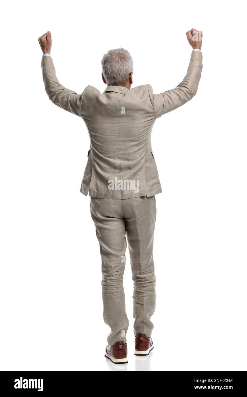 back view of old man in his 60s holding arms above head and cheering the victory on white background Stock Photo