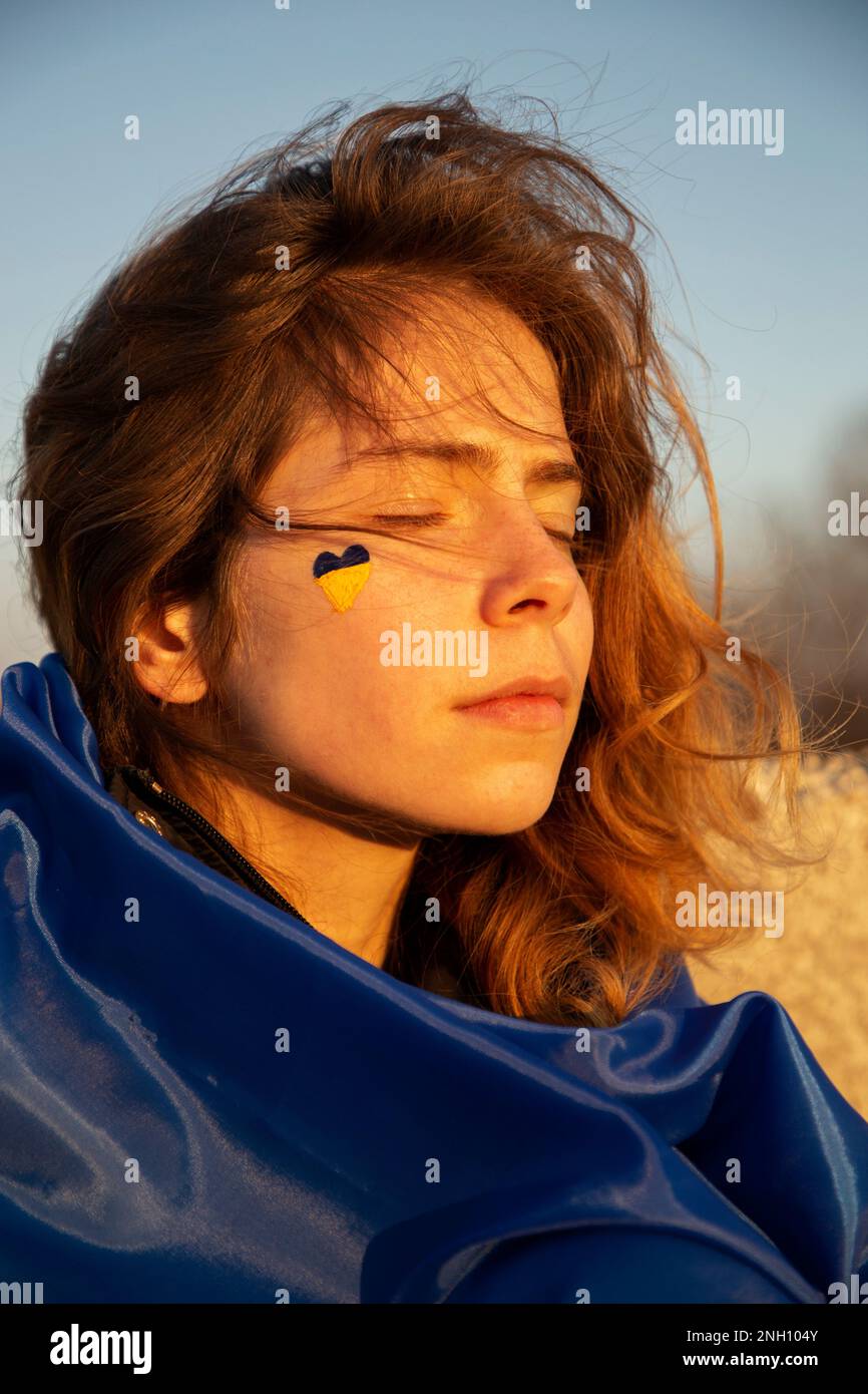 face portrait of a young beautiful tired woman 19 years old with a painted yellow-blue heart on her cheek. Support Ukraine. Stop the war. Belief in vi Stock Photo