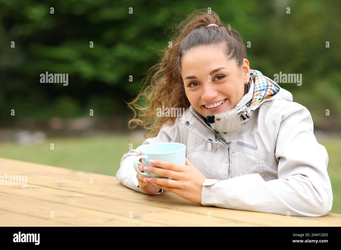Woman in a picnic table drinking coffee in the mountain looking at camera Stock Photo