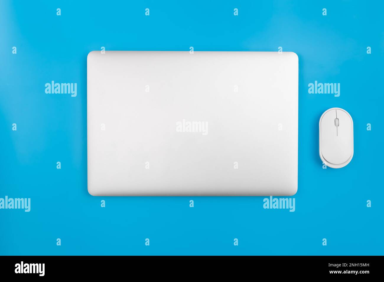 Closed laptop and computer mouse on a blue background, top view. Stock Photo