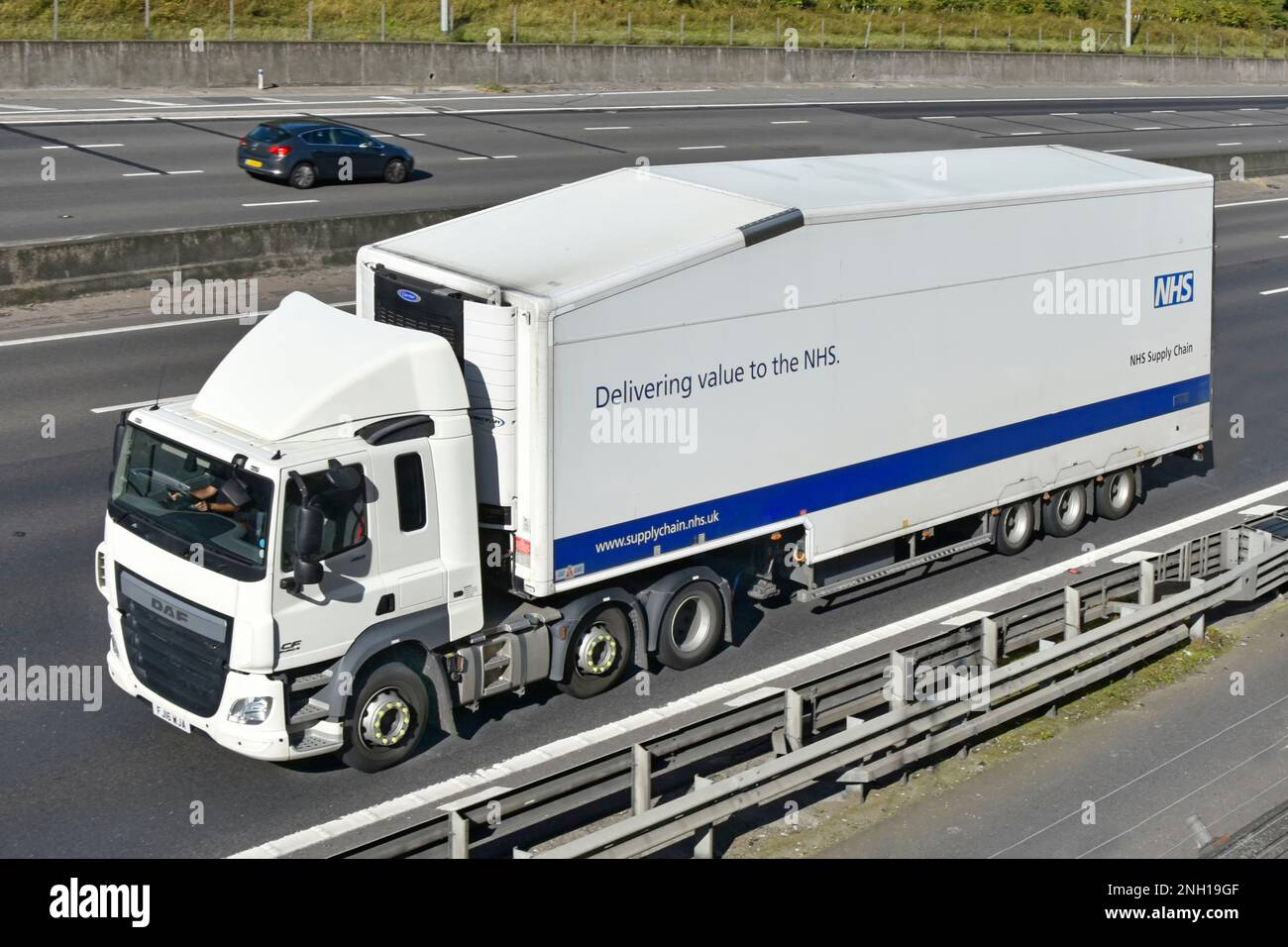 Side front aerial view of National Health Service healthcare supply chain DAF CF hgv NHS lorry truck & driver articulated trailer driving UK motorway Stock Photo