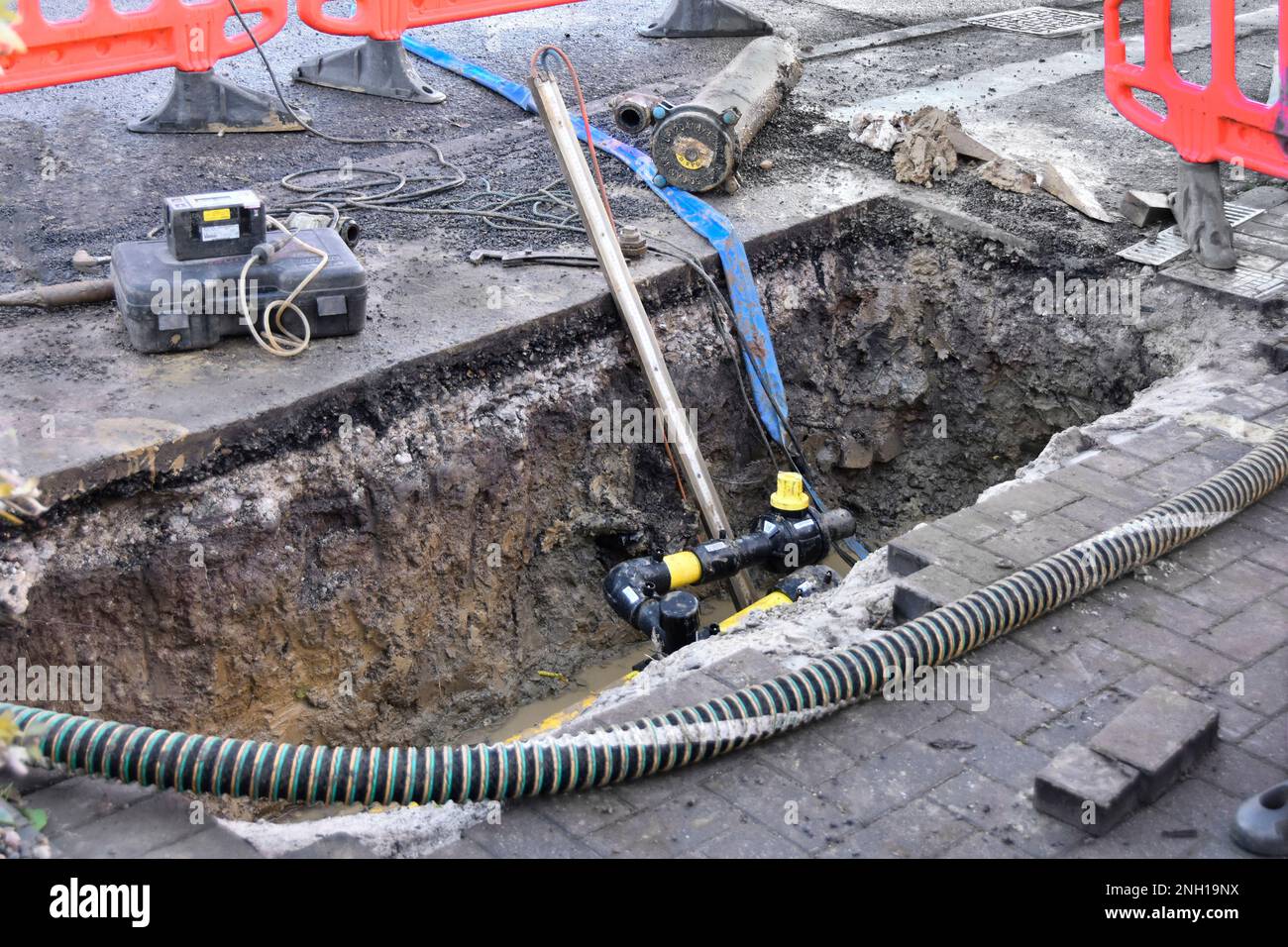 Gas street main renew & trench across house drive contractor equipment & work to remove section old steel pipe temp flexible hose maintains supply UK Stock Photo