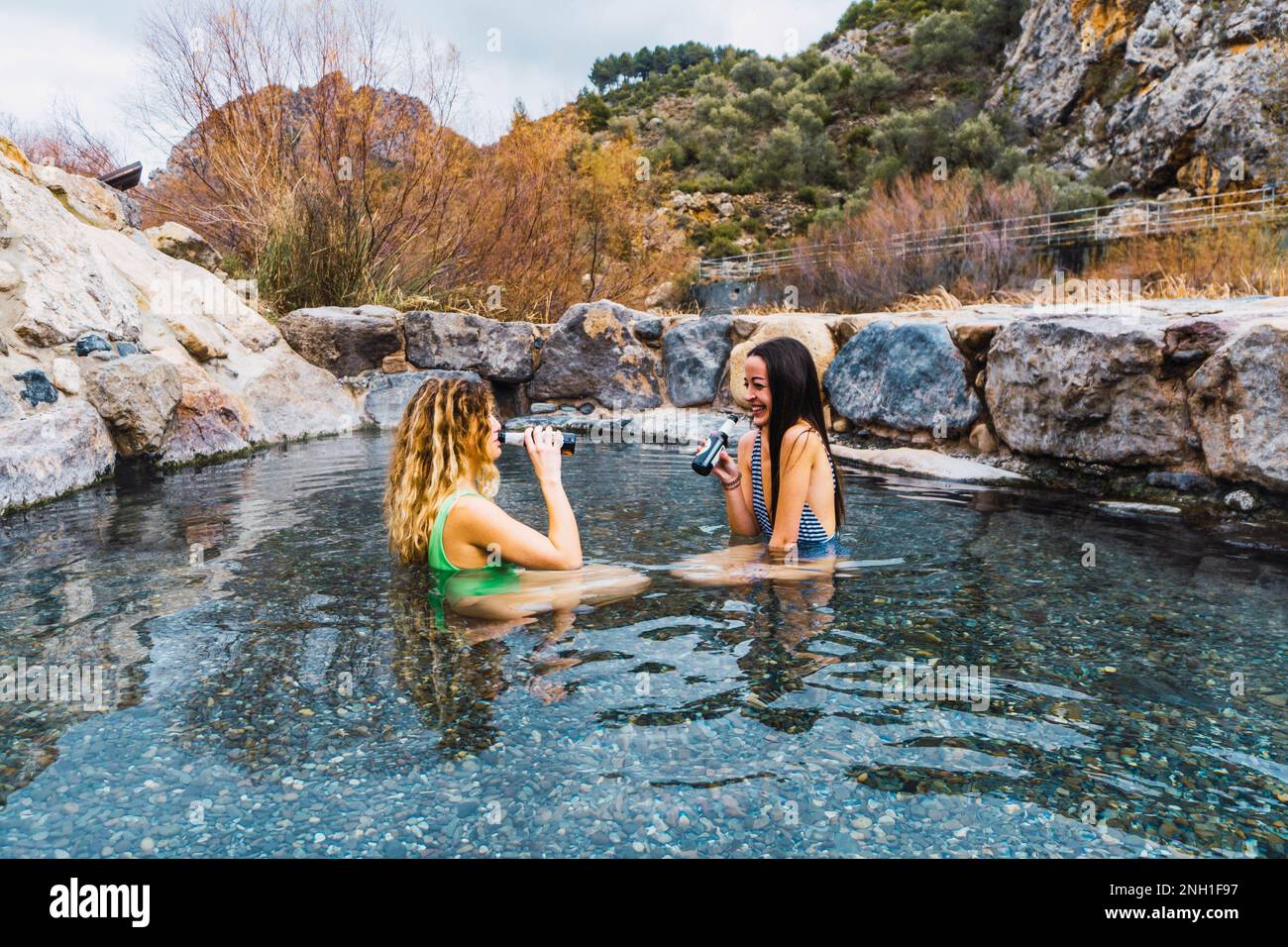 two people relaxing in natural hot springs drinking beer Stock Photo
