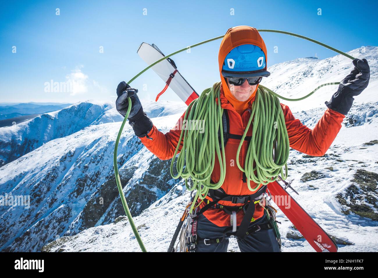 Ski mountaineer coiling rope with snowy mountains behind Stock Photo