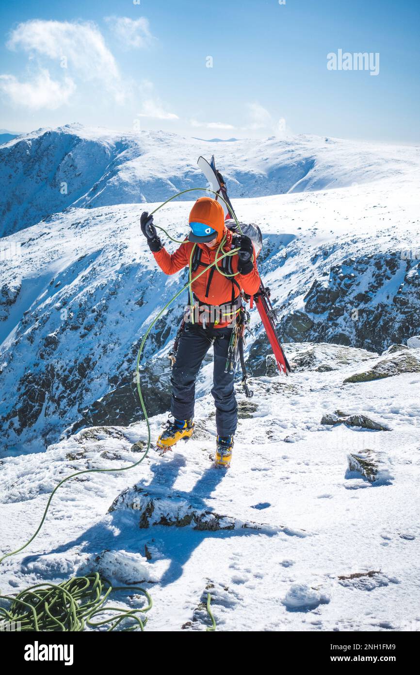 Ski mountaineer coiling rope with snowy mountains behind Stock Photo