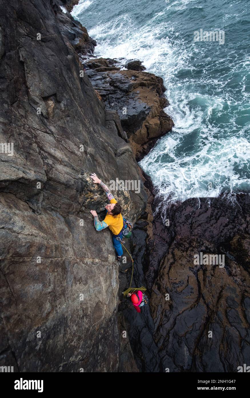 Man rock climbing on seaside cliff with waves crashing below Stock