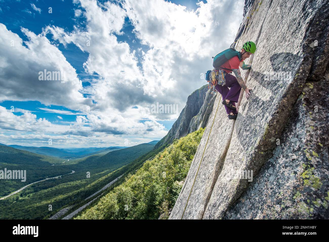 Man rock climbing steep crack on cliff with valley behind Stock Photo