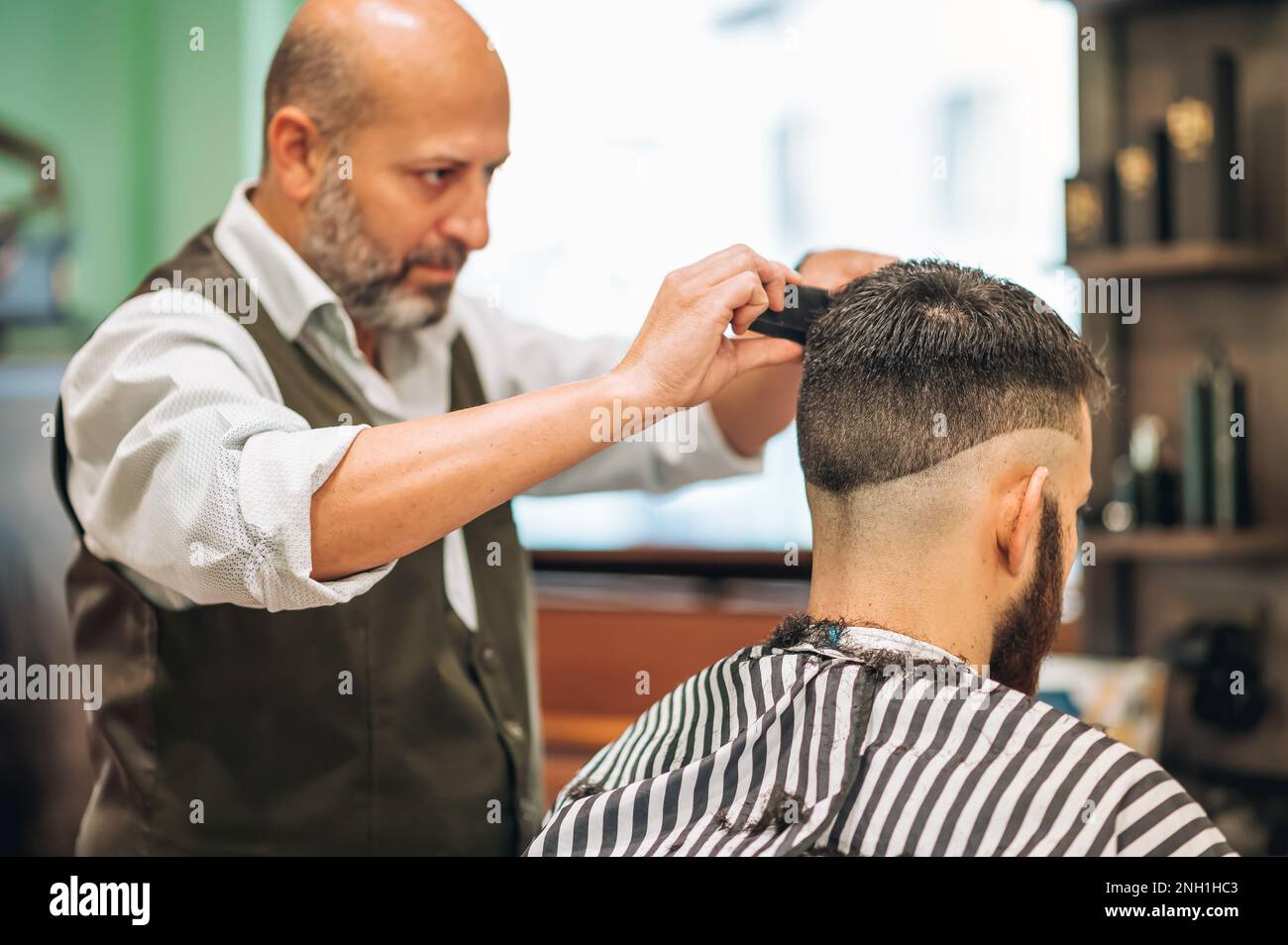 Aged bearded male barber with comb and scissors doing haircut to man in contemporary salon Stock Photo