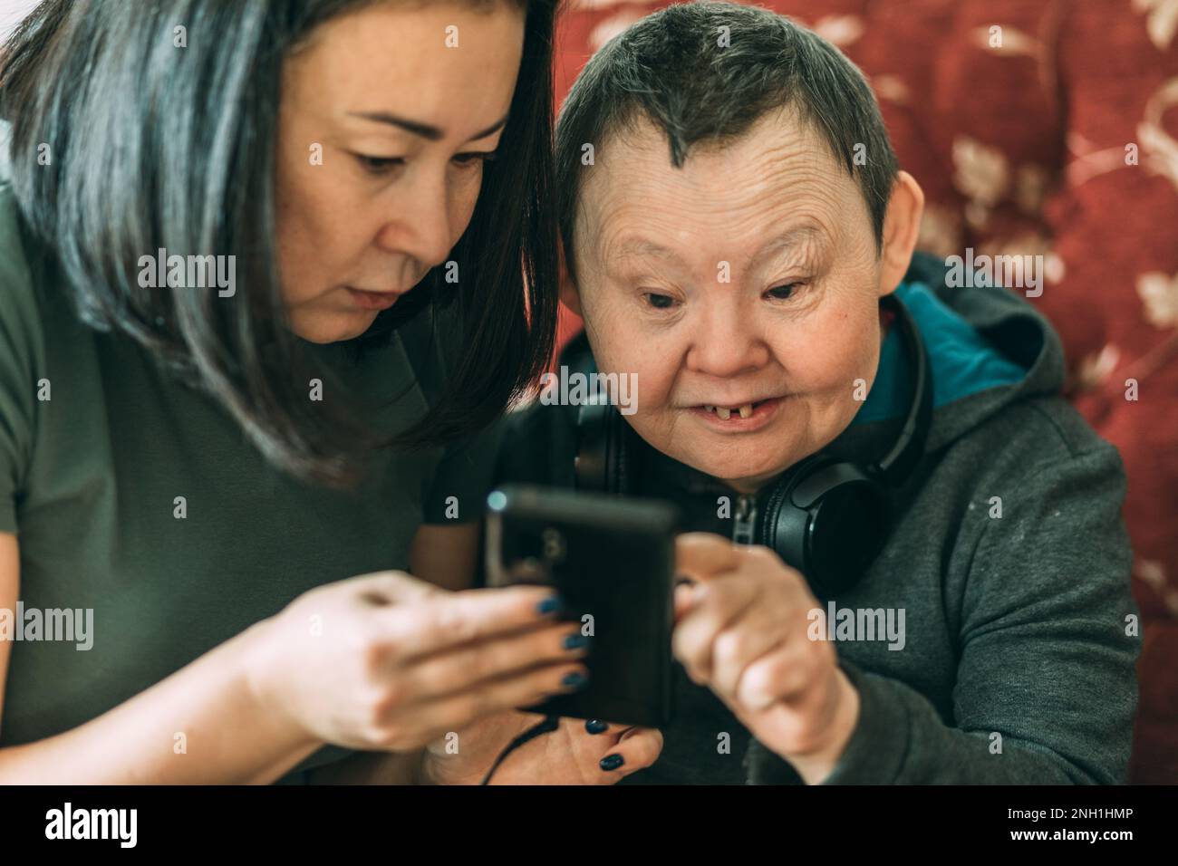 elderly woman with Down syndrome, asian assistant helps to use phone