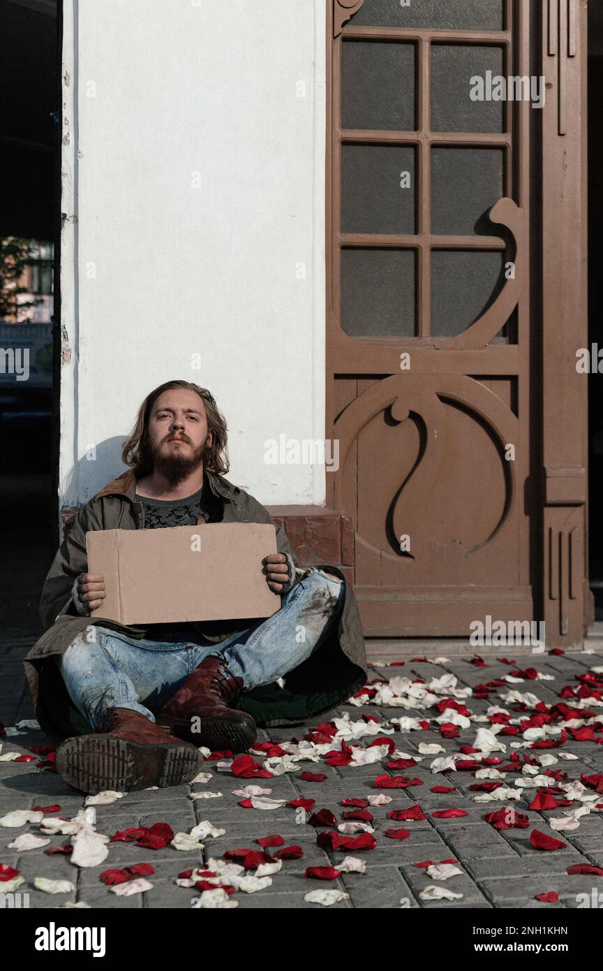 homeless man is sitting on the ground where rose petals are scattered Stock Photo