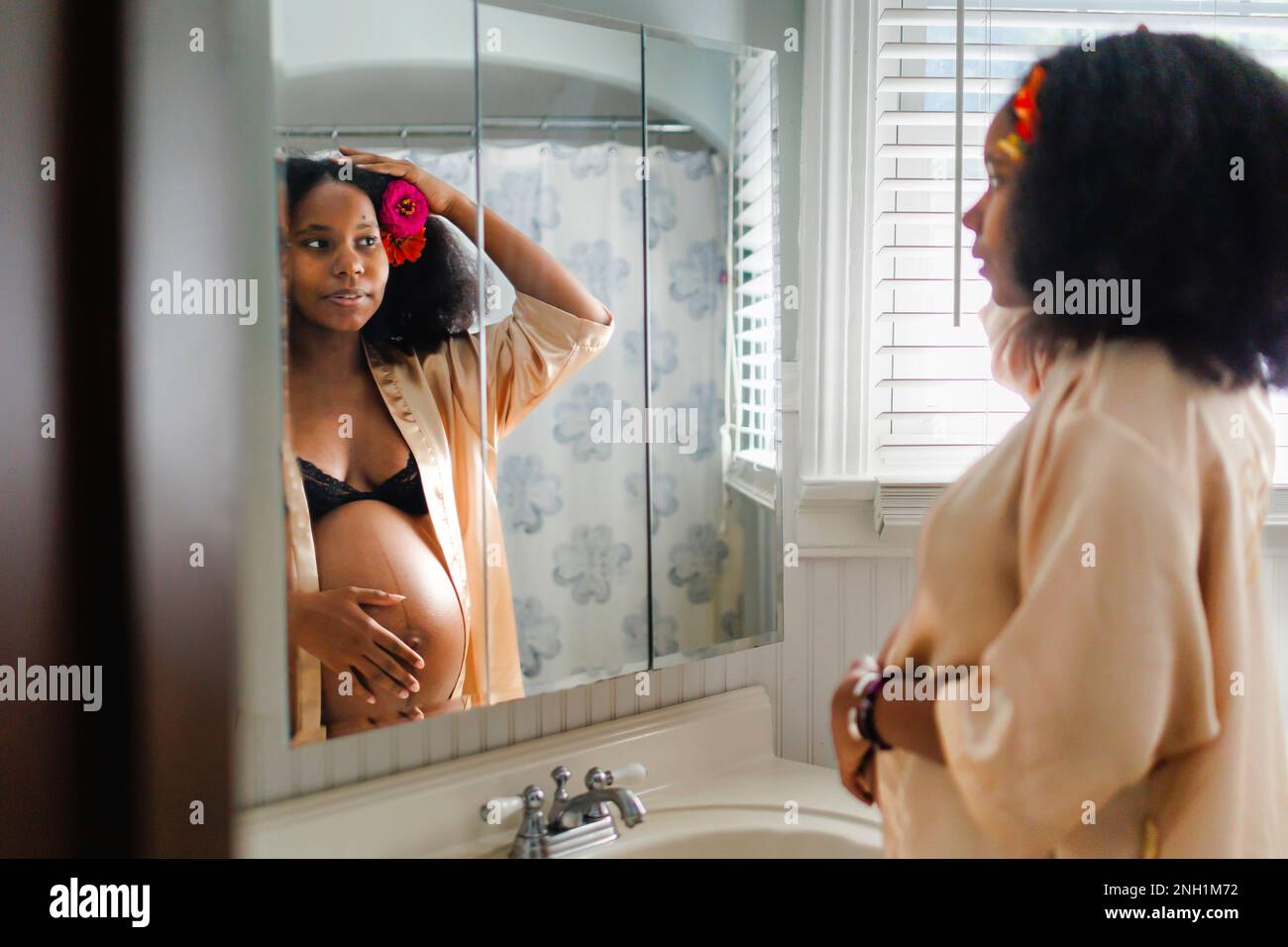 A young pregnant woman looks at herself in mirror Stock Photo