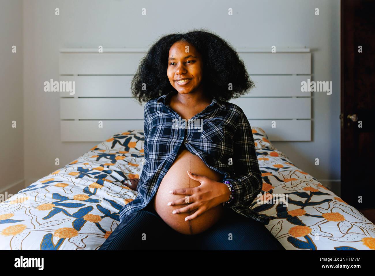 A young woman sits on bed holding pregnant belly Stock Photo