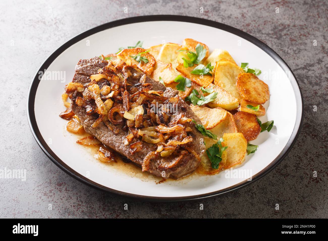 Original and Authentic German Zwiebelrostbraten with onion gravy and fried potatoes Bratkartoffeln closeup on the plate on the table. Horizontal Stock Photo