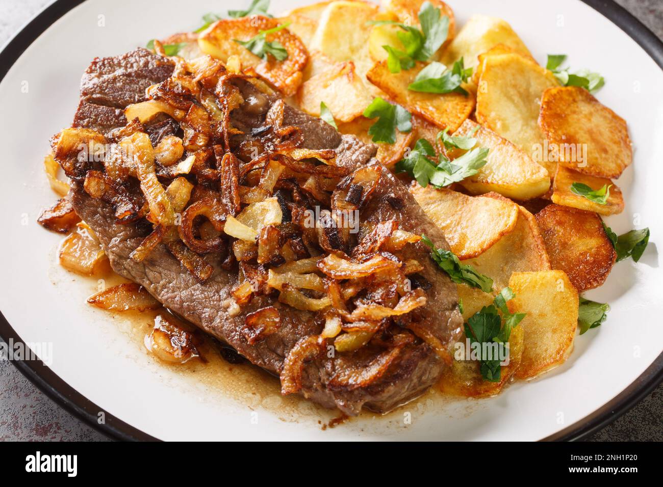 Roast Beef Zwiebelrostbraten with onions and fried potatoes Bratkartoffeln closeup on the plate on the table. Horizontal Stock Photo