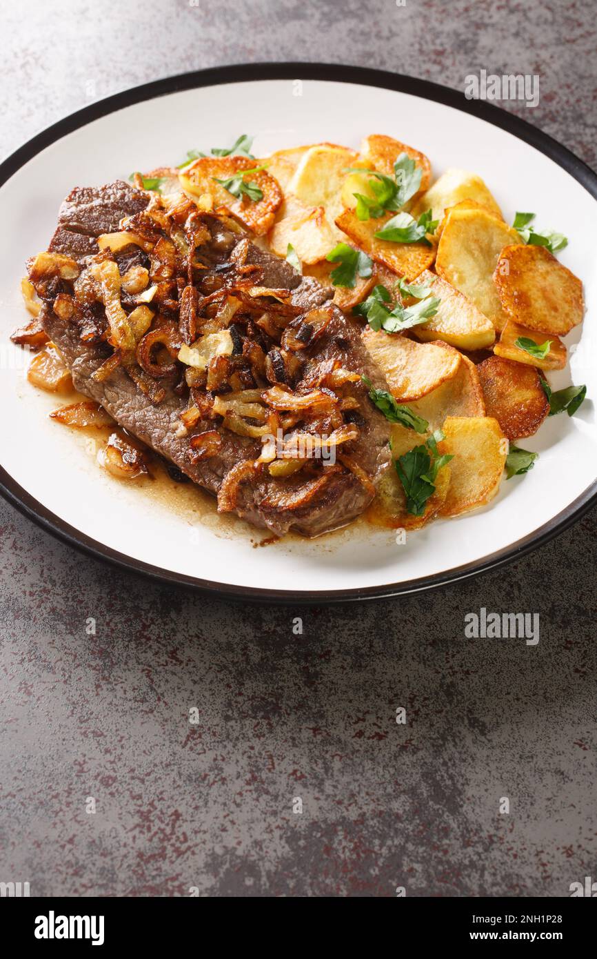 Zwiebelrostbraten a german steak with onions and fried potatoes Bratkartoffeln closeup on the plate on the table. Vertical Stock Photo