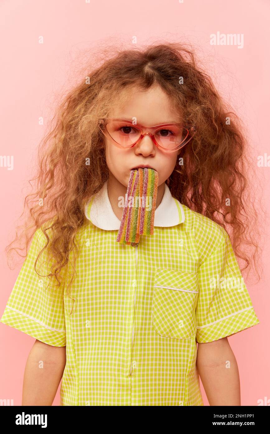 Little cute girl, child with curly hair posing in yellow dress, eating