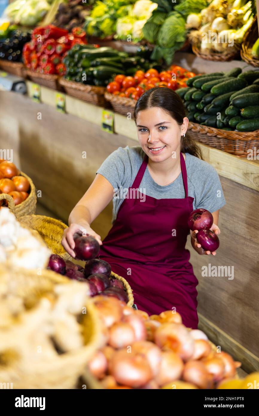 Female grocery store worker arranges red onion and other vegetables on