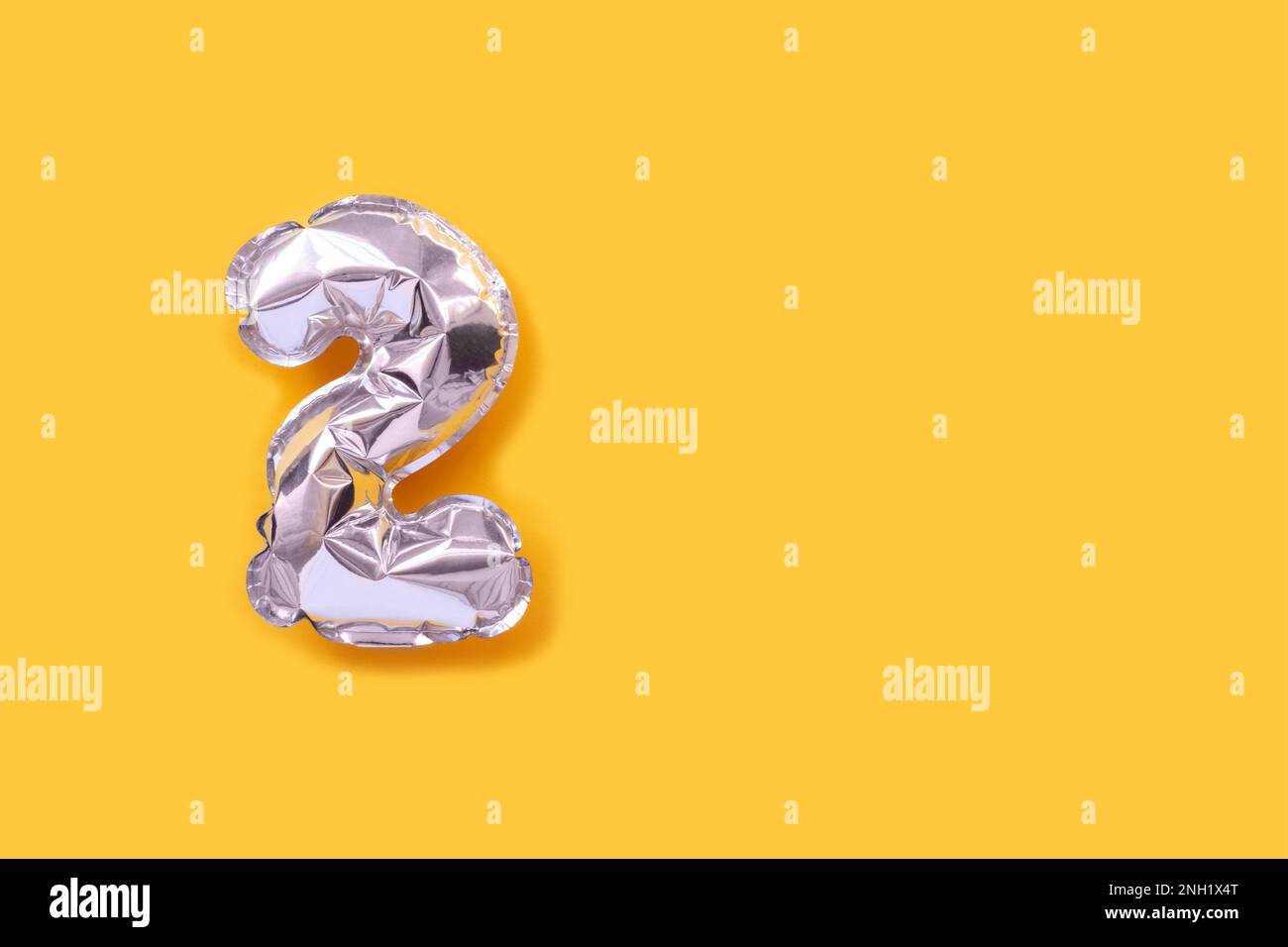 Number 2 silver balloons. Minimalistic composition with copy space on a yellow background. Stock Photo