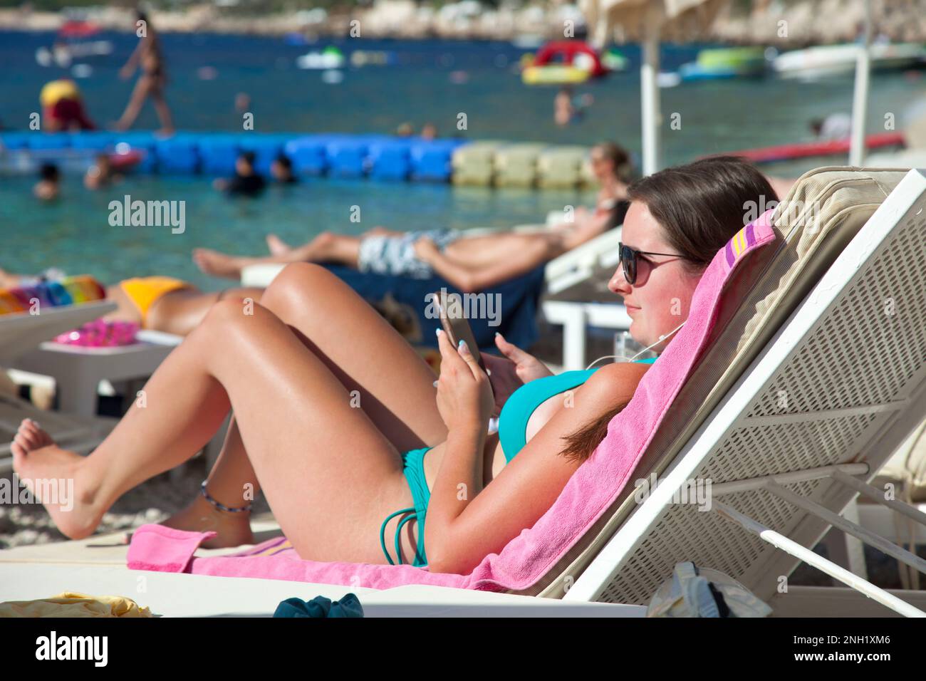 A young woman ( model released ) lying on a sun lounger holding a mobile phone at the Kalkan beach club, Kalkan, Turkey. July 2022 Stock Photo