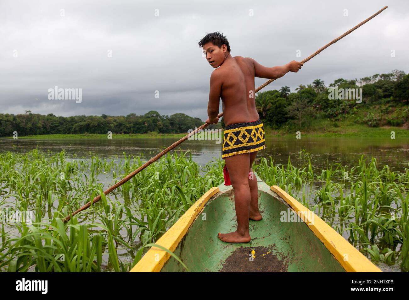 A young indigenous Embera man in traditional dress guides the dugout canoe through shallow water in Lake Alajuela in Panama. Stock Photo
