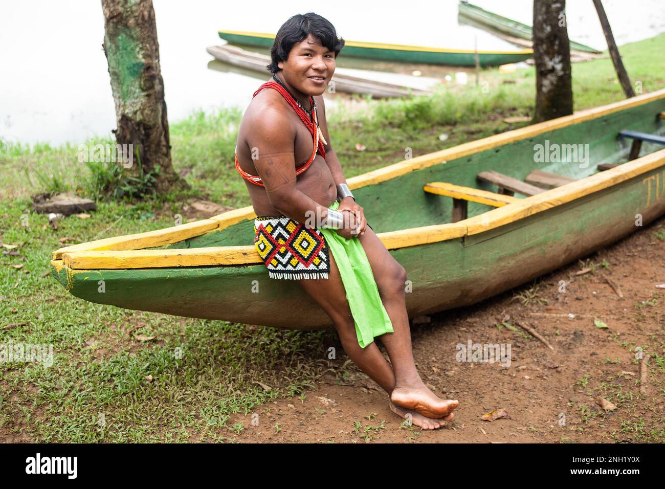 An indigenous Embera man in traditional dress in Panama sits on a 30 foot long dugout canoe or cayuco, hand-hewn from a single tree. Stock Photo