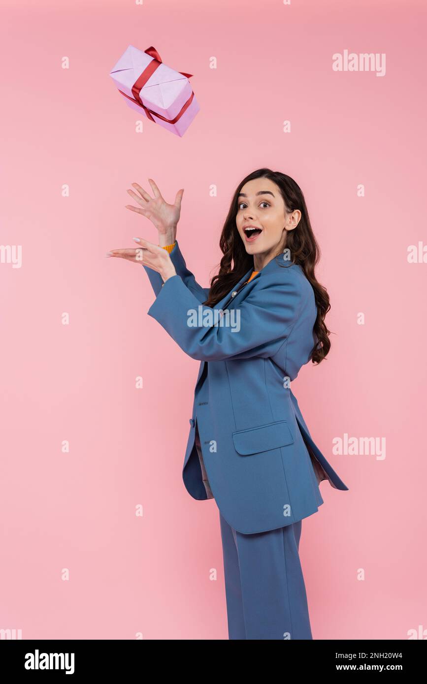 amazed young woman in blue blazer catching wrapped present isolated on pink,stock image Stock Photo