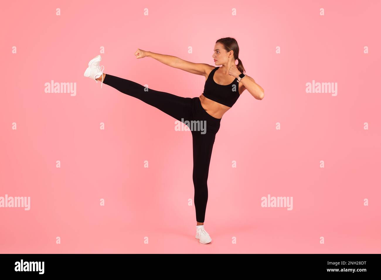 Motivated Young Woman Doing Karate Side Kick Move On Pink Studio Background Stock Photo