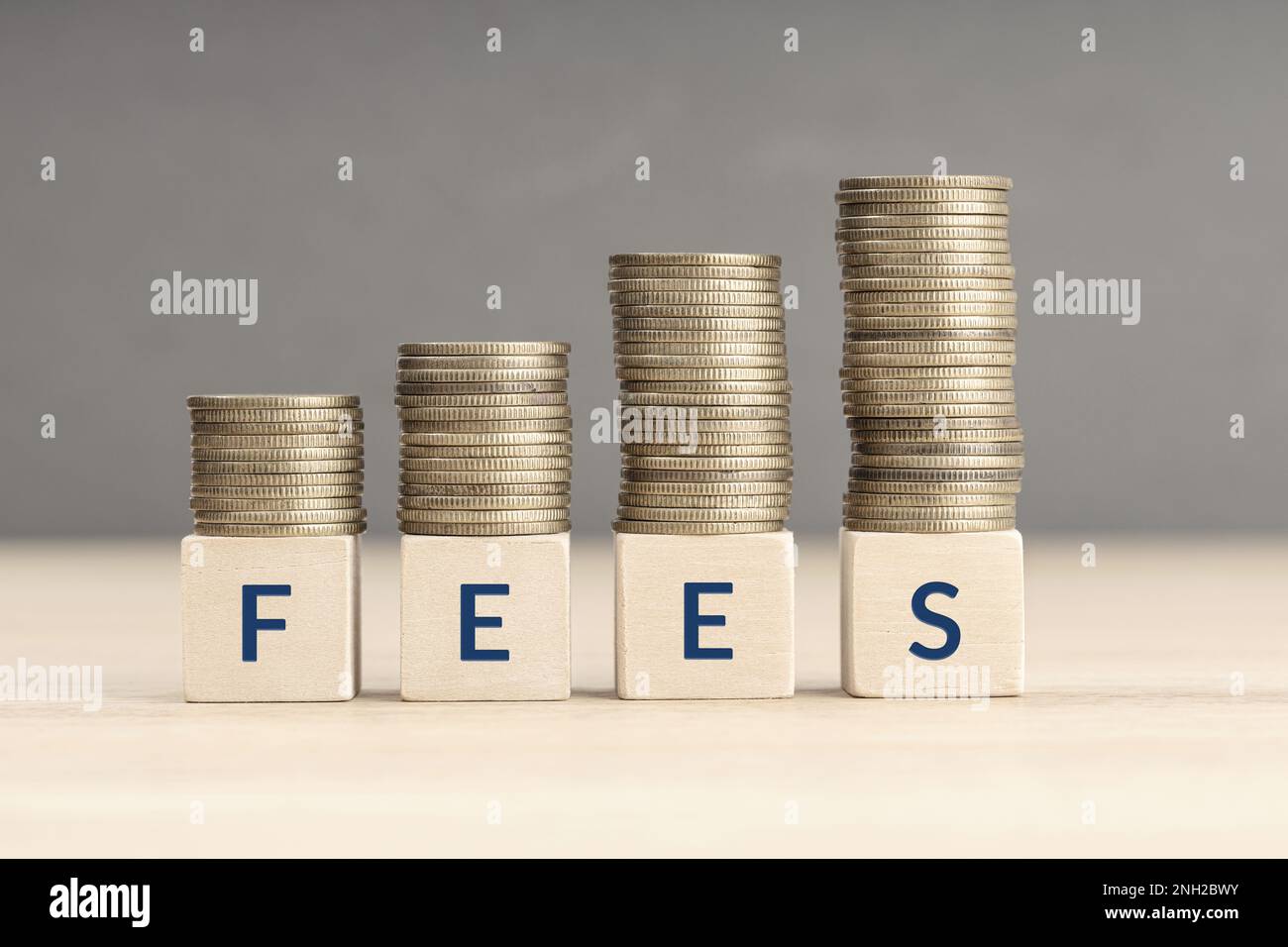Fees increasing concept. Text word on wooden blocks with coins stacked in increasing stacks. Copy space Stock Photo