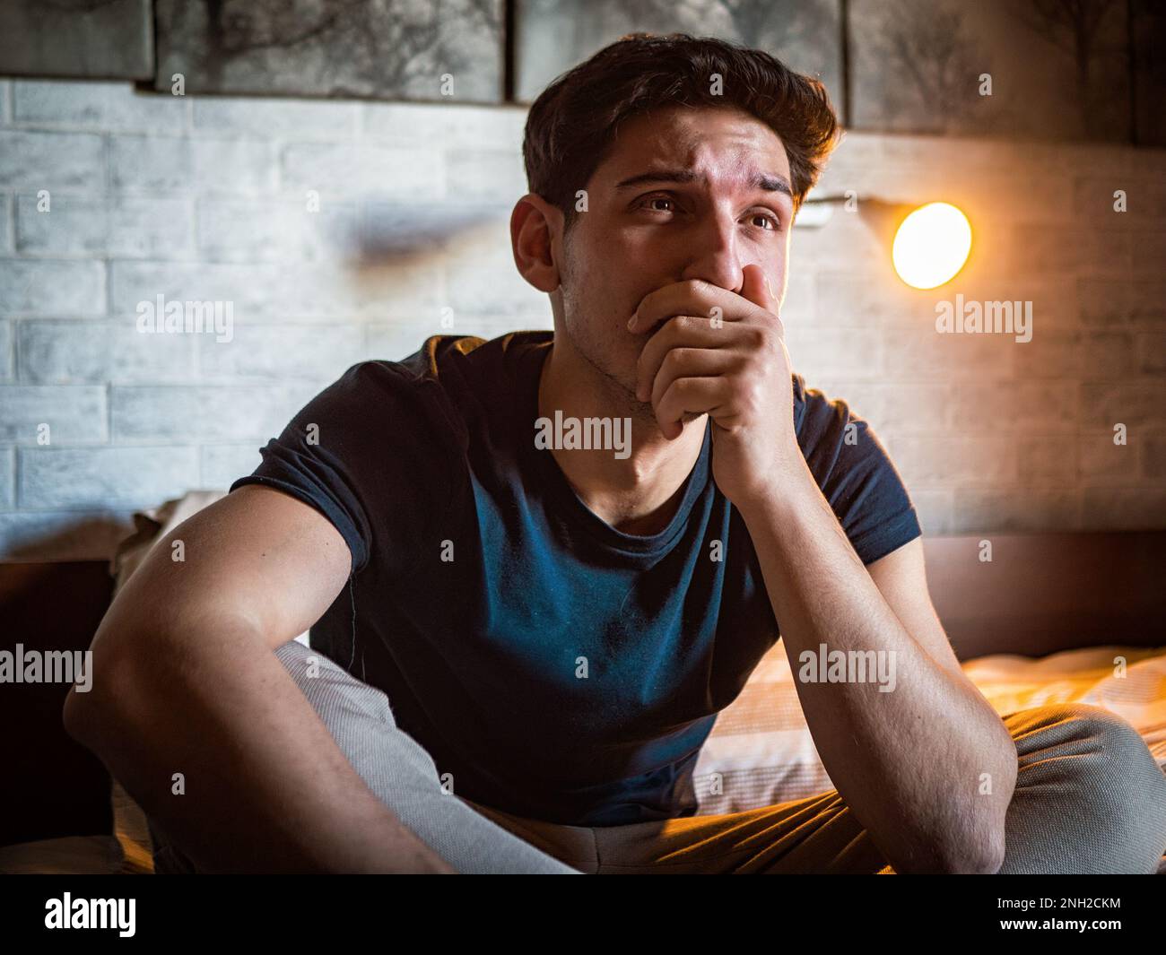 Man covering mouth while sitting on bed crying Stock Photo Alamy