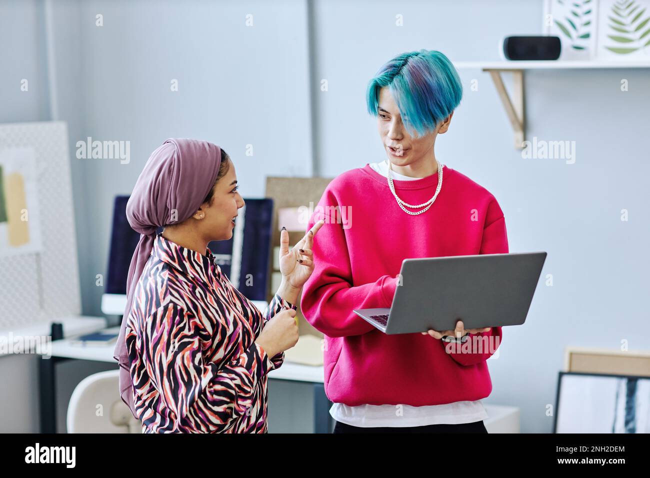 Waist up portrait of creative gen Z team discussing project while standing in office and holding laptop Stock Photo