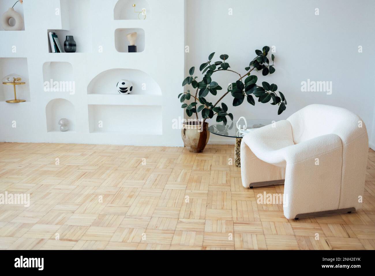 Modern interior with white walls and light parquet. Designer table consists of a glass top and two natural stones. There are fluffy armchair in the sh Stock Photo