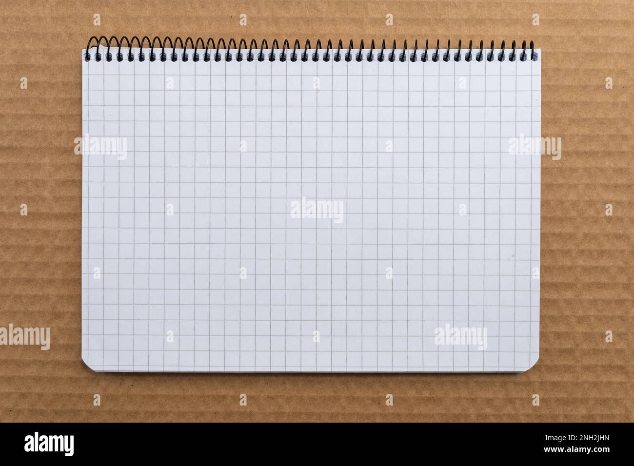 Graph paper spiral Notebook on top of brown cardboard, top view. Stock Photo
