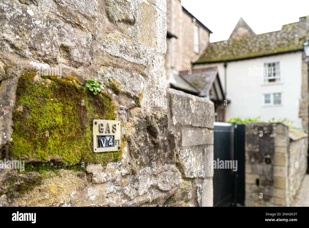 Shallow focus of a mains gas location marker built into a medieval stone wall. A nearby town house is visible. Stock Photo