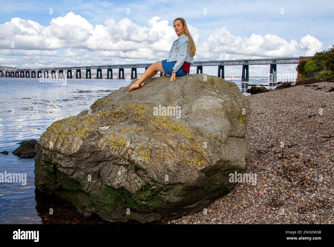 On a beautiful October day in Wormit Beach, Fife, Rhianna Martin sits on large rocks beside the River Tay, Scotland Stock Photo