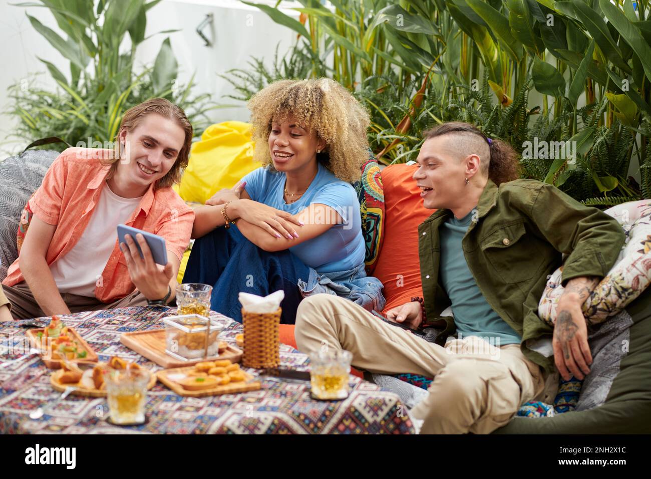 Cheerful young man showing funny video on smartphone to friends when they are hanging out together Stock Photo