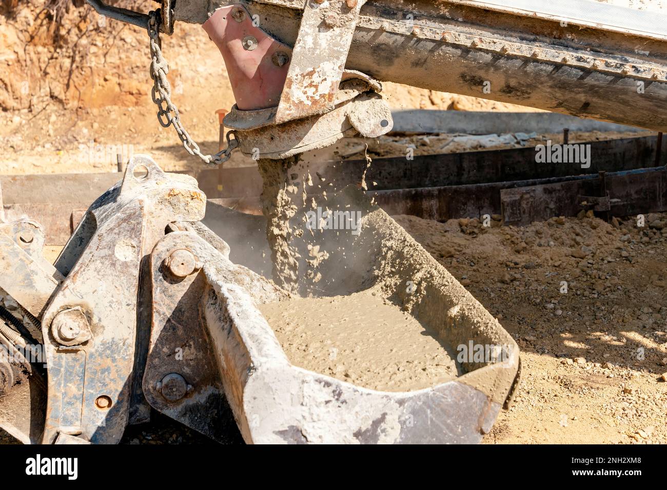 Concrete mixer truck pouring fresh wet concrete into excavators bucket at a construction site Stock Photo