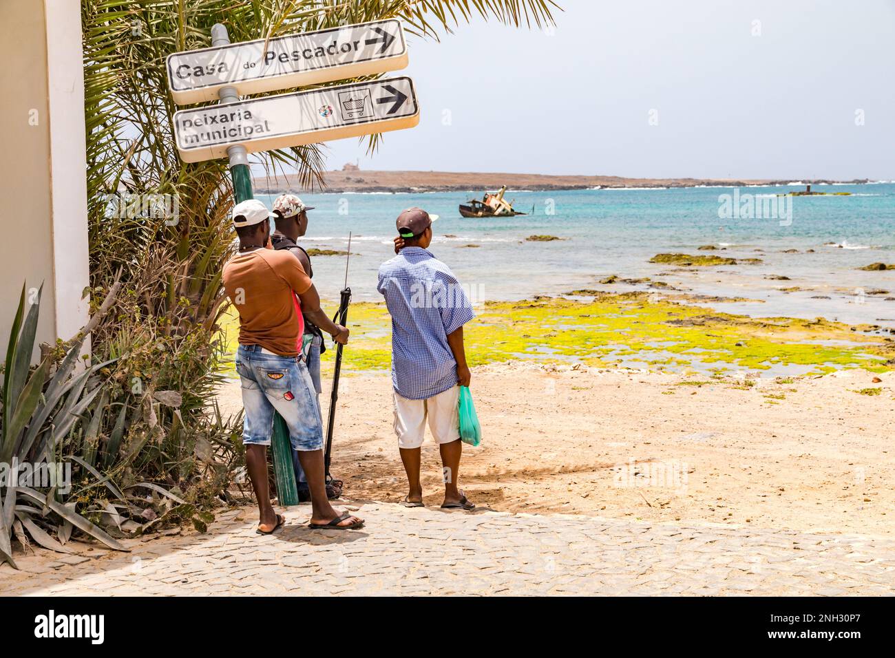 Three men at the harbor of Sal Rei look at the Atlantic Ocean, Boa Vista, Cape Verde Islands Stock Photo