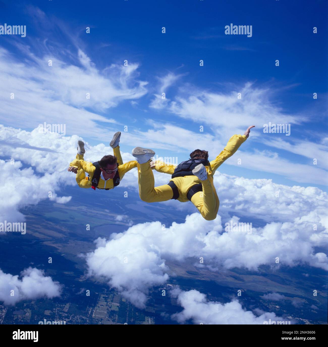 To skydivers freefalling while holding hands above the clouds Stock
