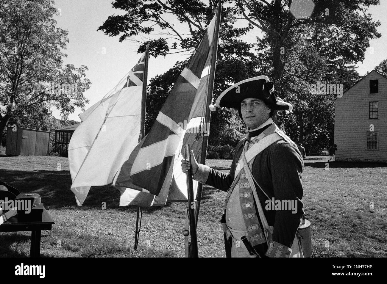 A Red Coat (British) soldier stands in front of flags in a camp during