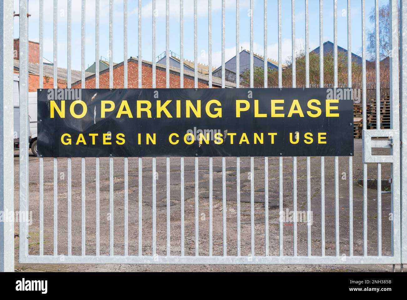 Large yellow and black sign on metal gate saying no parking please gates in constant use Stock Photo