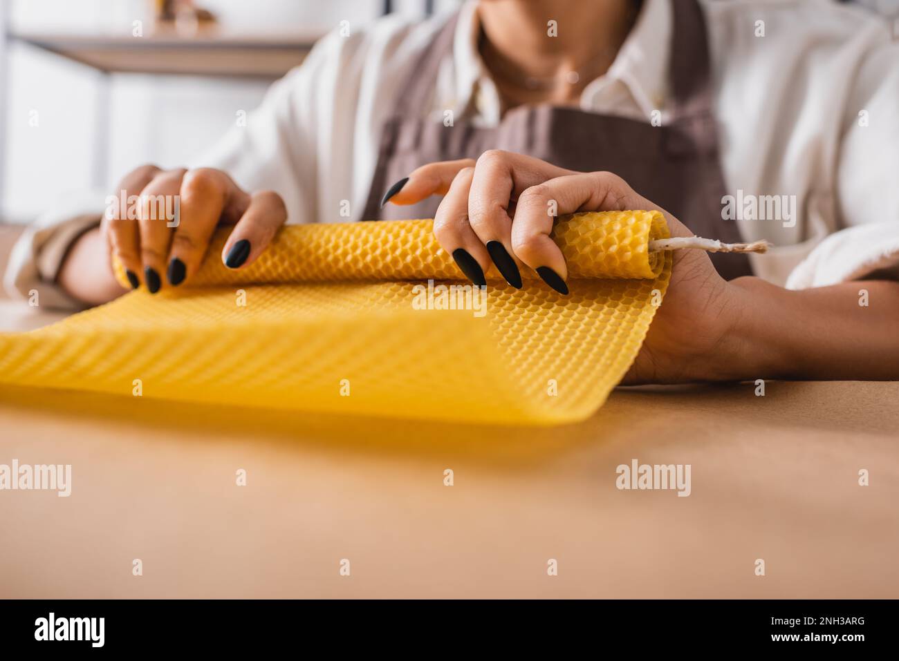 partial view of blurred african american woman making candle and rolling wax sheet in craft workshop,stock image Stock Photo