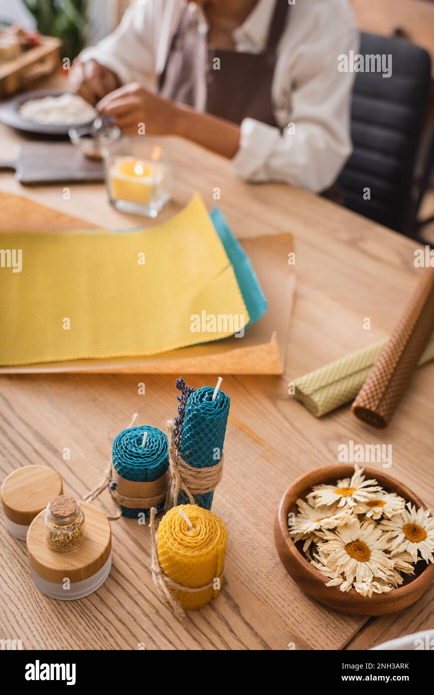 dried camomiles and homemade candles near wax sheets and cropped african american craftswoman on blurred background,stock image Stock Photo