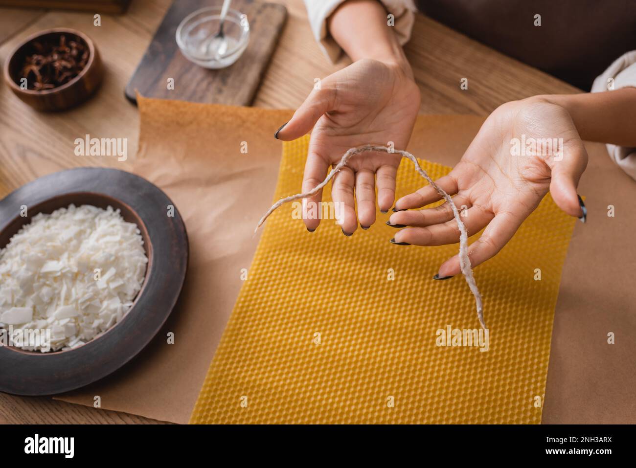 partial view of african american woman holding twine near wax sheet and wooden plate with grated beeswax in workshop,stock image Stock Photo